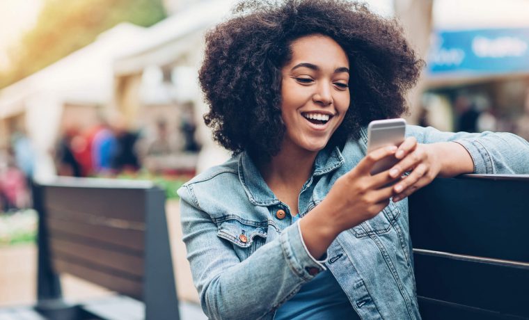 Mulher sentada mexendo em seu celular, abrindo um SMS Marketing