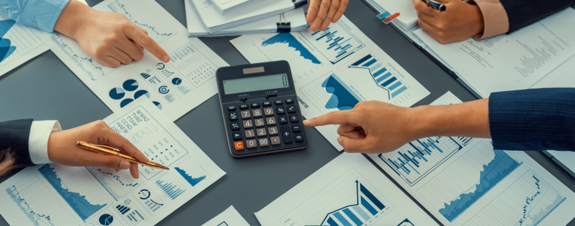 Pessoas analisando relatórios financeiros e gráficos ao redor de uma calculadora, representando o controle e o planejamento do fluxo de caixa de uma empresa.