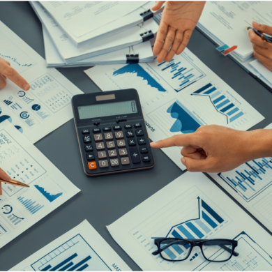 Pessoas analisando relatórios financeiros e gráficos ao redor de uma calculadora, representando o controle e o planejamento do fluxo de caixa de uma empresa.