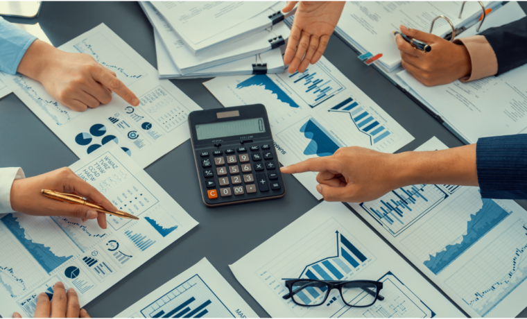 Pessoas analisando relatórios financeiros e gráficos ao redor de uma calculadora, representando o controle e o planejamento do fluxo de caixa de uma empresa.
