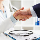 Médico apertando a mão de um empresário em um ambiente profissional, representando a parceria entre empresa e serviço de saúde por meio de um plano de saúde empresarial.