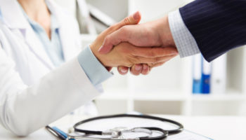 Médico apertando a mão de um empresário em um ambiente profissional, representando a parceria entre empresa e serviço de saúde por meio de um plano de saúde empresarial.