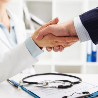 Médico apertando a mão de um empresário em um ambiente profissional, representando a parceria entre empresa e serviço de saúde por meio de um plano de saúde empresarial.