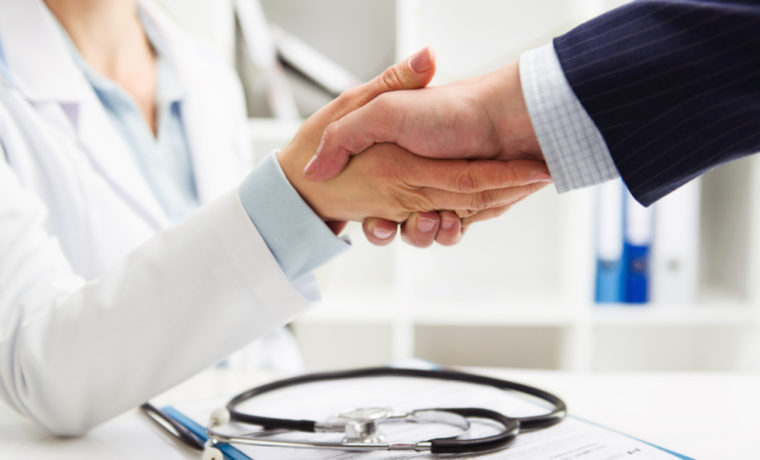 Médico apertando a mão de um empresário em um ambiente profissional, representando a parceria entre empresa e serviço de saúde por meio de um plano de saúde empresarial.