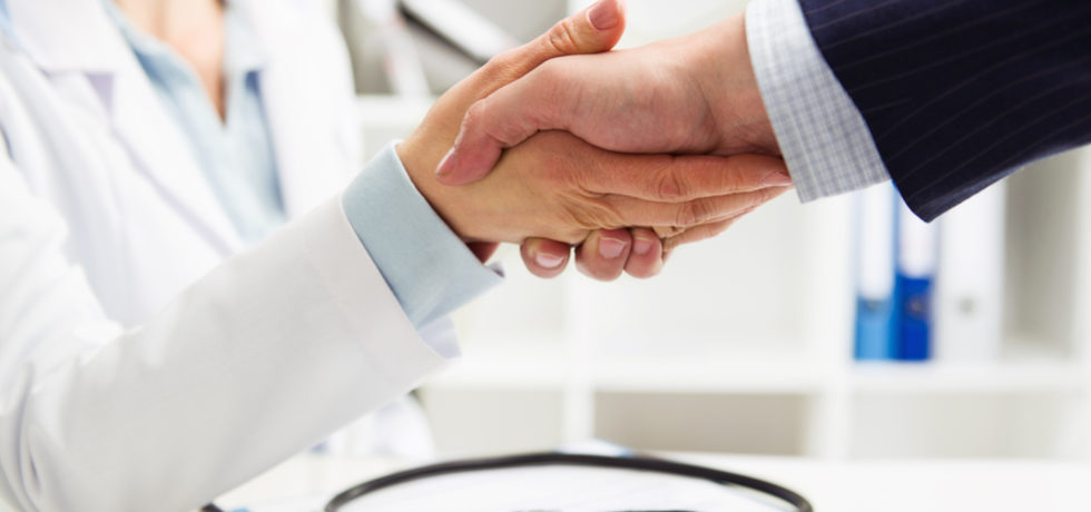 Médico apertando a mão de um empresário em um ambiente profissional, representando a parceria entre empresa e serviço de saúde por meio de um plano de saúde empresarial.
