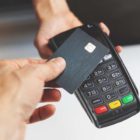 Pessoa realizando um pagamento com cartão em uma maquininha, representando as transações por cartão e as taxas cobradas nas operações comerciais.