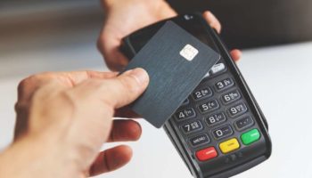 Pessoa realizando um pagamento com cartão em uma maquininha, representando as transações por cartão e as taxas cobradas nas operações comerciais.