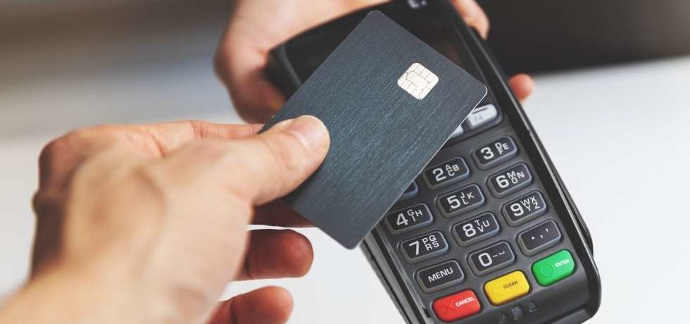 Pessoa realizando um pagamento com cartão em uma maquininha, representando as transações por cartão e as taxas cobradas nas operações comerciais.