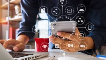Pessoa a usar smartphone e computador portátil, com ícones digitais interligados sobrepostos.