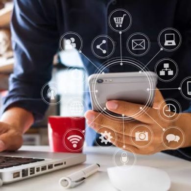 Pessoa a usar smartphone e computador portátil, com ícones digitais interligados sobrepostos.