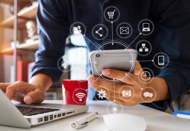Pessoa a usar smartphone e computador portátil, com ícones digitais interligados sobrepostos.