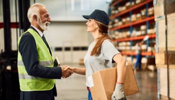 Fornecedor e profissional do setor logístico apertam as mãos em um centro de distribuição, simbolizando parceria comercial e negociação com fornecedores.