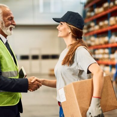 Fornecedor e profissional do setor logístico apertam as mãos em um centro de distribuição, simbolizando parceria comercial e negociação com fornecedores.