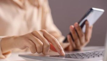 Pessoa utilizando um notebook e um celular para realizar atividades online, representando o uso de ferramentas digitais para vendas e pagamentos.