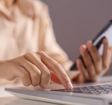 Pessoa utilizando um notebook e um celular para realizar atividades online, representando o uso de ferramentas digitais para vendas e pagamentos.
