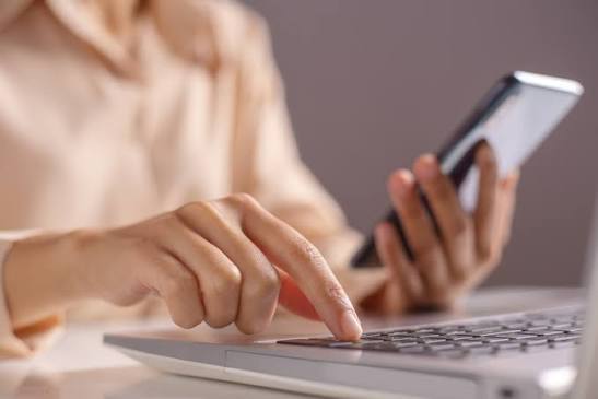 Pessoa utilizando um notebook e um celular para realizar atividades online, representando o uso de ferramentas digitais para vendas e pagamentos.